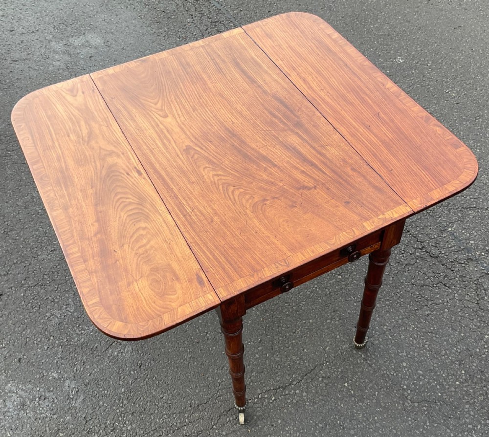 A Georgian mahogany Pembroke table featuring two hinged drop leaves, a crossbanded timber border, ring-turned legs, and brass castors. View IX