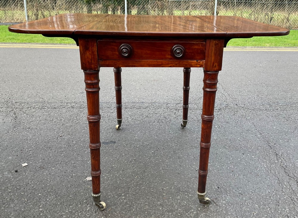 A Georgian mahogany Pembroke table featuring two hinged drop leaves, a crossbanded timber border, ring-turned legs, and brass castors. View X