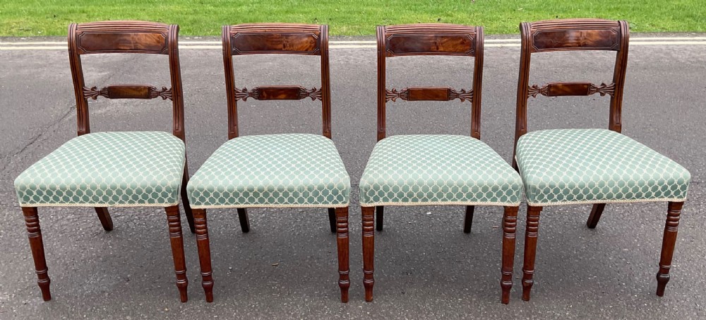A set of four antique Georgian mahogany dining chairs with flame mahogany top rails, carved crossbars, turned front legs, and green pattern upholstered seats.