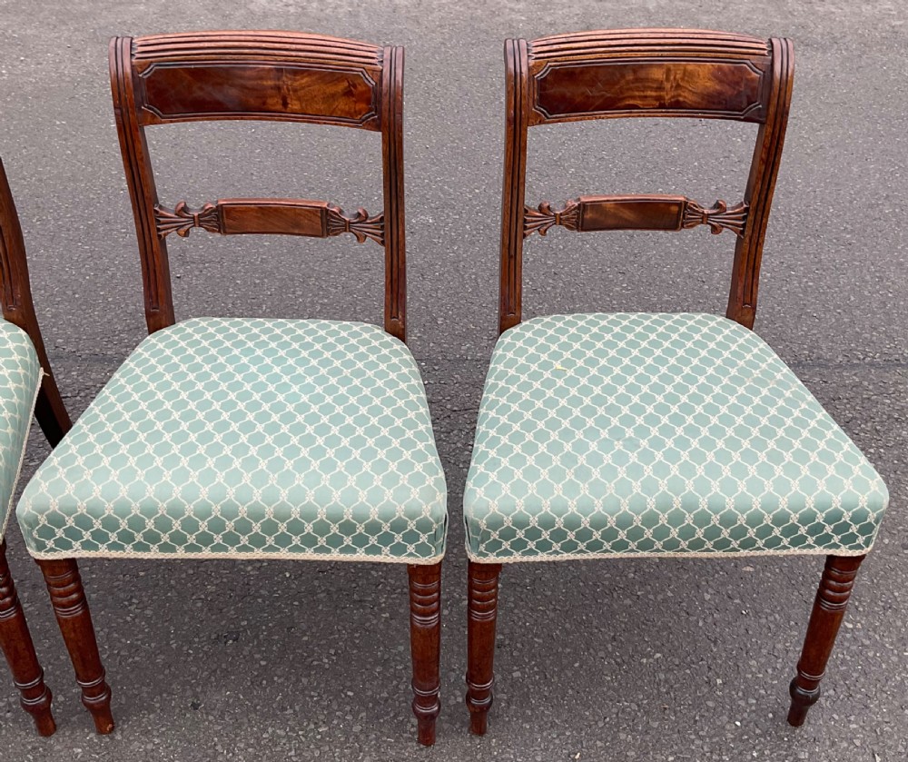 A set of four antique Georgian mahogany dining chairs with flame mahogany top rails, carved crossbars, turned front legs, and green pattern upholstered seats. View V