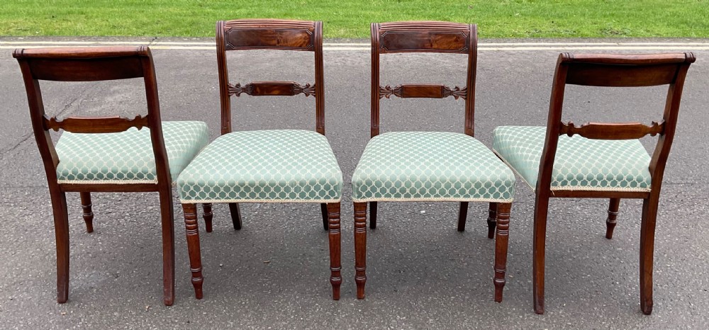A set of four antique Georgian mahogany dining chairs with flame mahogany top rails, carved crossbars, turned front legs, and green pattern upholstered seats. View VII