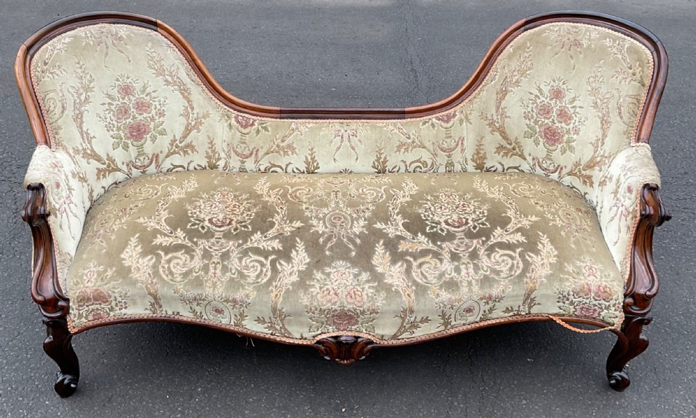 A Victorian upholstered settee featuring a carved mahogany frame with dual contoured backrests and olive green floral patterned fabric.
