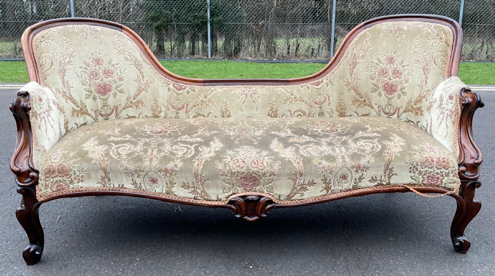 A Victorian upholstered settee featuring a carved mahogany frame with dual contoured backrests and olive green floral patterned fabric. View II