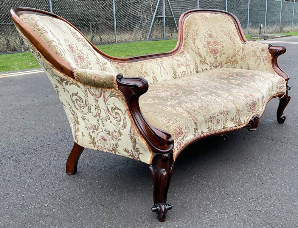 A Victorian upholstered settee featuring a carved mahogany frame with dual contoured backrests and olive green floral patterned fabric. View III