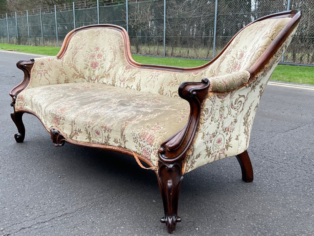 A Victorian upholstered settee featuring a carved mahogany frame with dual contoured backrests and olive green floral patterned fabric. View VI