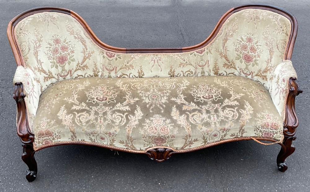 A Victorian upholstered settee featuring a carved mahogany frame with dual contoured backrests and olive green floral patterned fabric. View VII