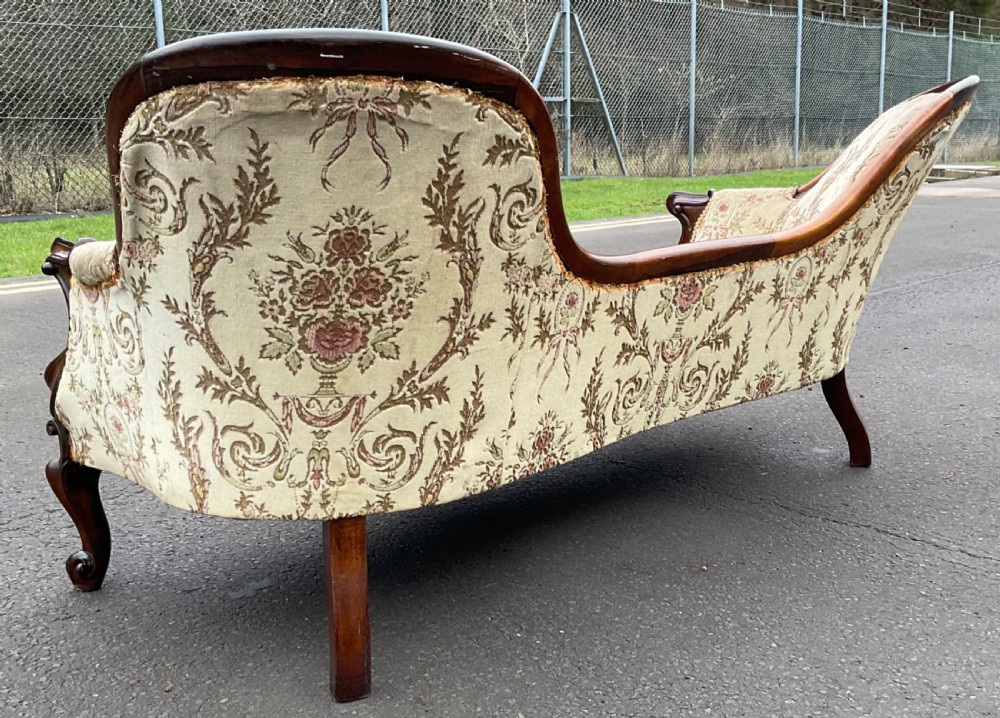 A Victorian upholstered settee featuring a carved mahogany frame with dual contoured backrests and olive green floral patterned fabric. View IX