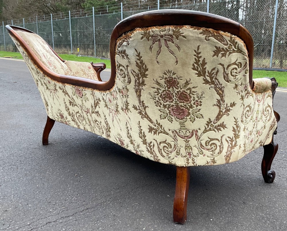 A Victorian upholstered settee featuring a carved mahogany frame with dual contoured backrests and olive green floral patterned fabric. View X