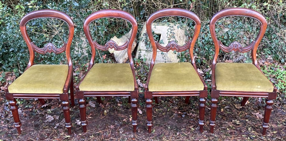 A set of four Victorian mahogany dining chairs featuring rounded balloon backs with carved central splats and olive green velvet upholstered seats.