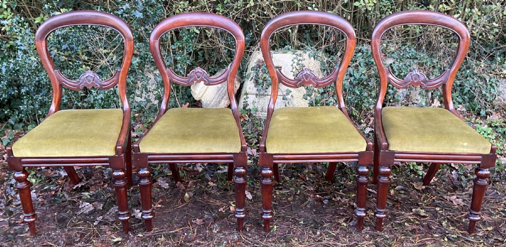 A set of four Victorian mahogany dining chairs featuring rounded balloon backs with carved central splats and olive green velvet upholstered seats. View V