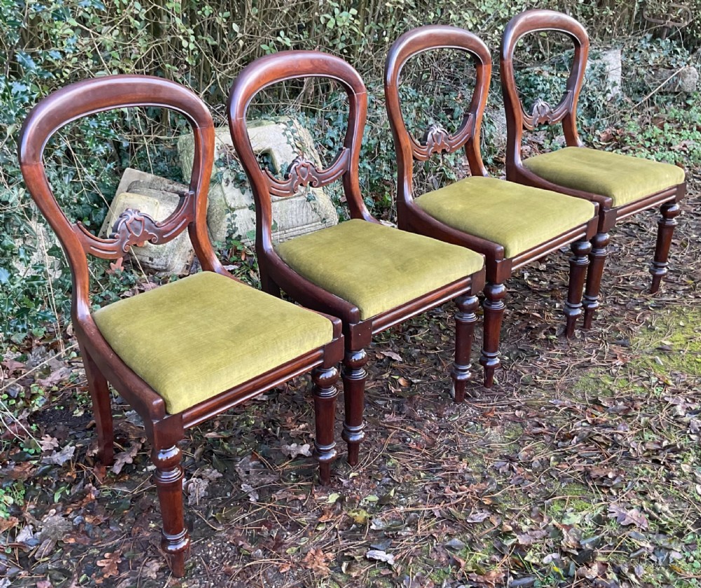 A set of four Victorian mahogany dining chairs featuring rounded balloon backs with carved central splats and olive green velvet upholstered seats. View VI