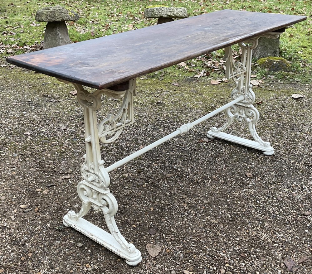 A long Victorian pub table featuring a dark wooden rectangular top supported by white painted decorative cast iron scrollwork legs and a central stretcher.