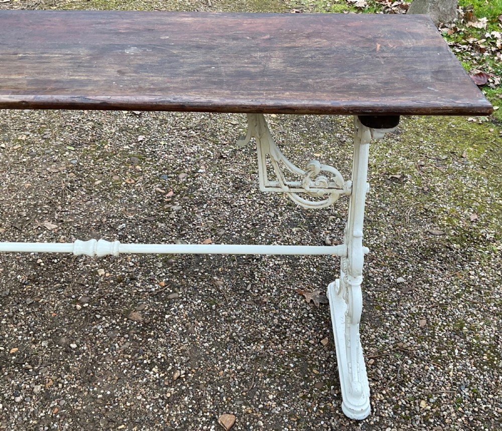 A long Victorian pub table featuring a dark wooden rectangular top supported by white painted decorative cast iron scrollwork legs and a central stretcher. View VI