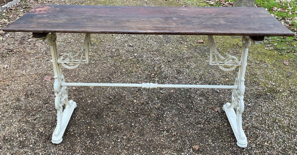 A long Victorian pub table featuring a dark wooden rectangular top supported by white painted decorative cast iron scrollwork legs and a central stretcher. View VII