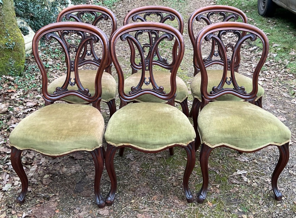 A set of six Victorian mahogany dining chairs featuring carved balloon back frames, cabriole front legs, and green velvet upholstered seats.