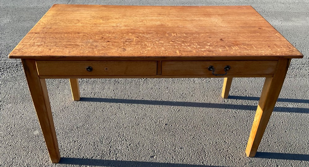 A large golden oak writing table featuring a flat rectangular top, two front drawers with metal pull handles, and four straight tapered legs.