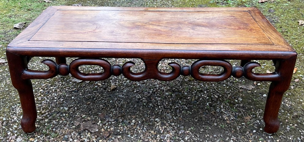 A low rectangular oriental hardwood coffee table featuring an intricately carved openwork apron and curved legs.