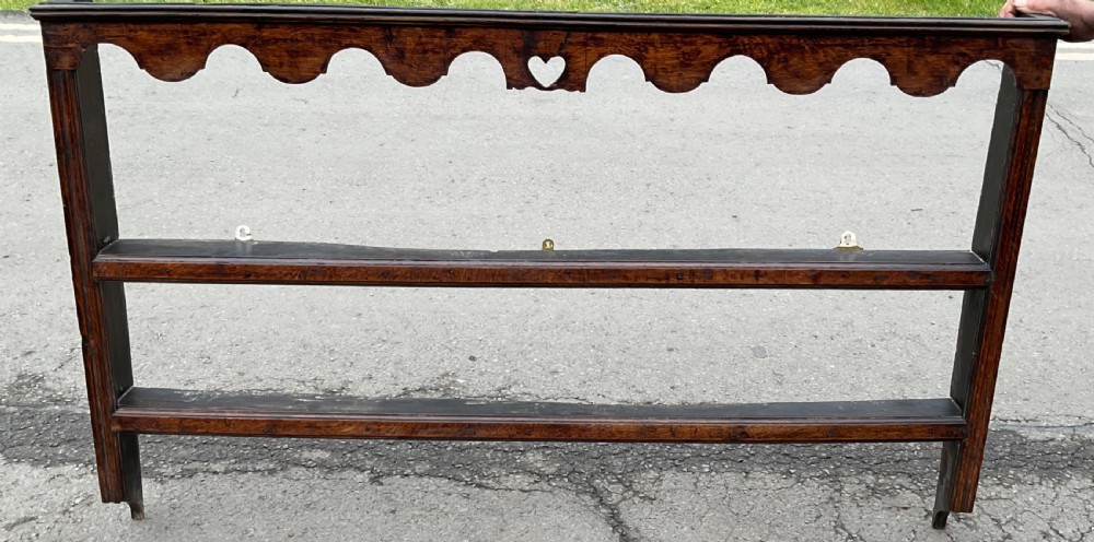A dark oak wall shelf unit featuring two open tiers, a scalloped top frieze, and a central heart cutout motif.