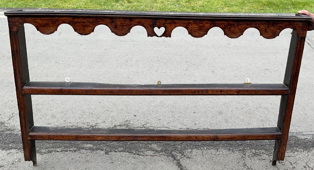 A dark oak wall shelf unit featuring two open tiers, a scalloped top frieze, and a central heart cutout motif. View V