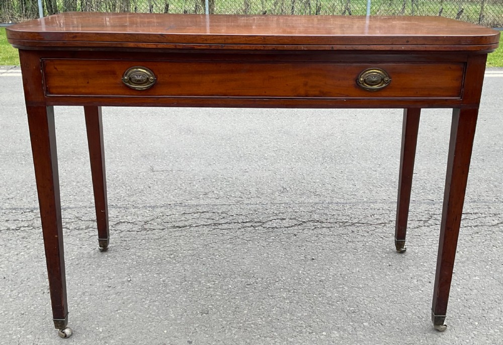 A Georgian mahogany card table featuring a rectangular fold-over top, a single long drawer with oval brass handles, tapered legs, and small brass castors. View III