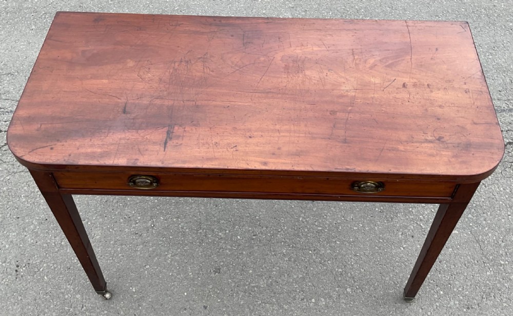 A Georgian mahogany card table featuring a rectangular fold-over top, a single long drawer with oval brass handles, tapered legs, and small brass castors. View V