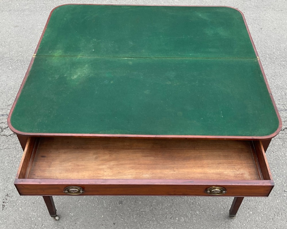 A Georgian mahogany card table featuring a rectangular fold-over top, a single long drawer with oval brass handles, tapered legs, and small brass castors. View VIII
