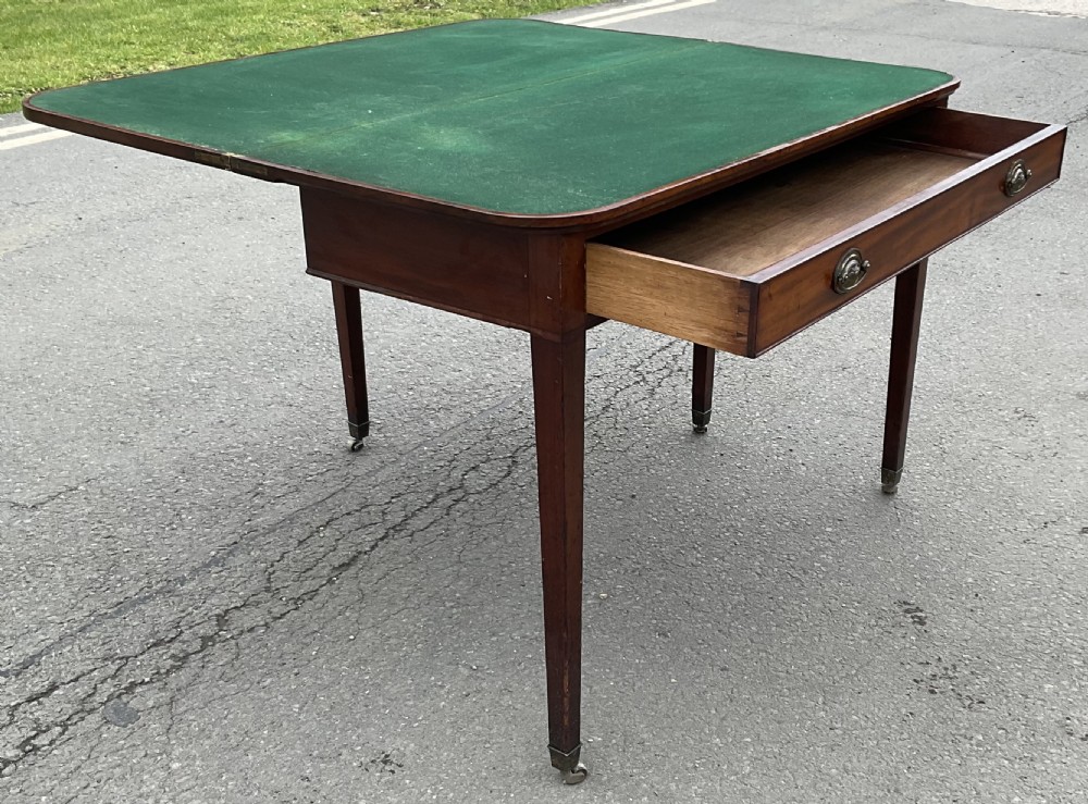 A Georgian mahogany card table featuring a rectangular fold-over top, a single long drawer with oval brass handles, tapered legs, and small brass castors. View IX