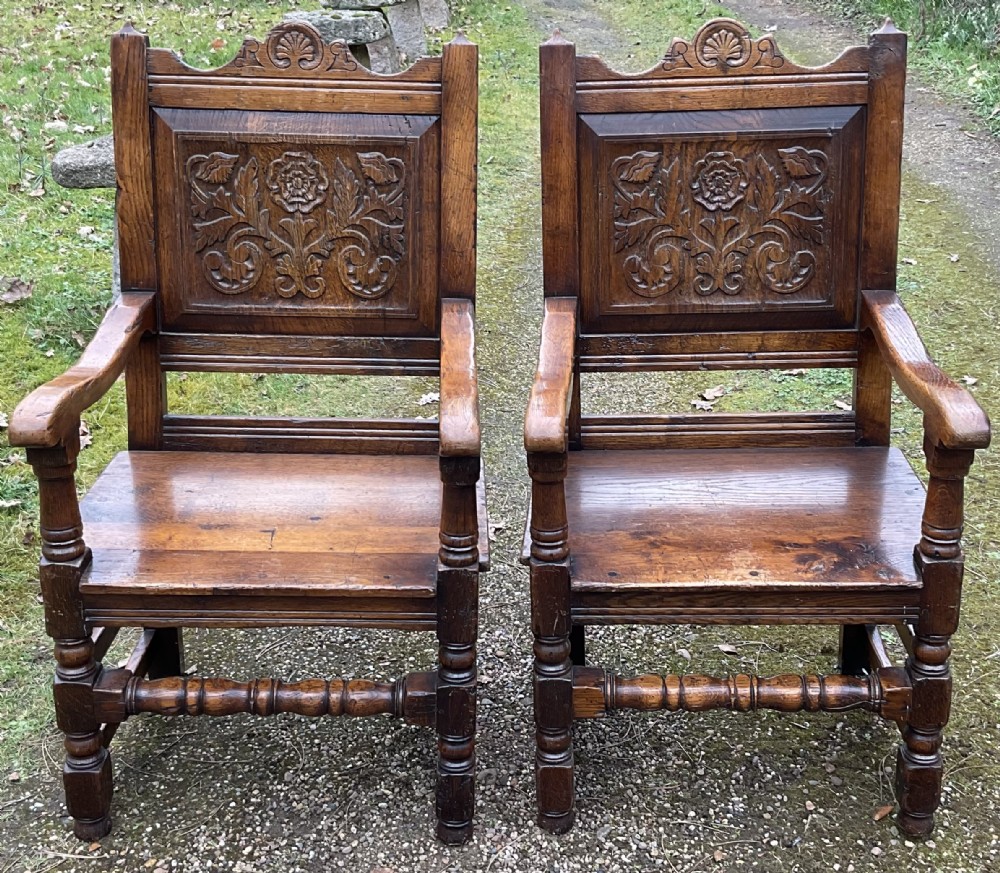 A pair of dark oak wainscot armchairs featuring carved floral back panels and turned legs.