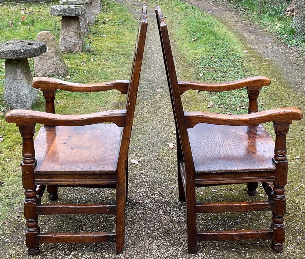 A pair of dark oak wainscot armchairs featuring carved floral back panels and turned legs. View V