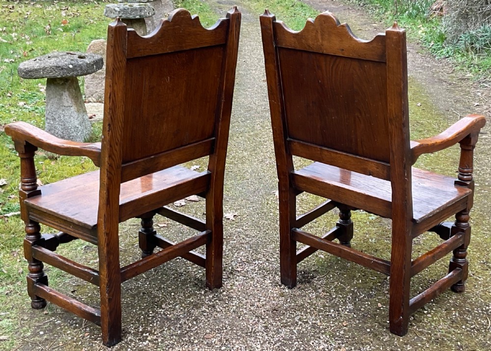 A pair of dark oak wainscot armchairs featuring carved floral back panels and turned legs. View VI