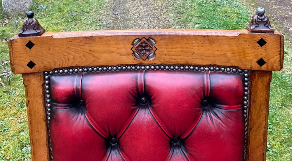 A Victorian Gothic Revival oak armchair featuring deep-buttoned red leather upholstery, carved finials, spindle arm supports, and turned legs with castors. View III