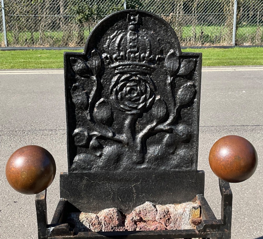 A black cast and wrought iron fire grate featuring a high backplate embossed with a crowned Tudor rose motif, brass sphere finials, and a front bar basket. View IV