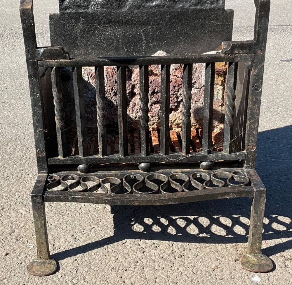 A black cast and wrought iron fire grate featuring a high backplate embossed with a crowned Tudor rose motif, brass sphere finials, and a front bar basket. View VI
