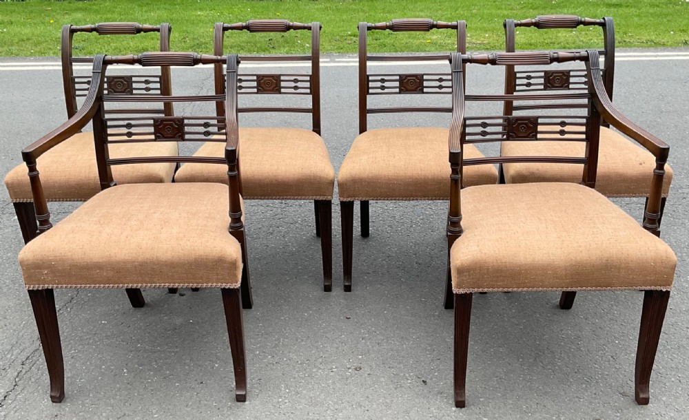 Set of six dark mahogany Georgian dining chairs featuring reeded frames, carved bar backs, and beige fabric seats.