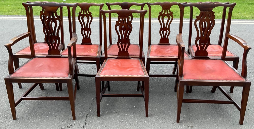 A set of eight Edwardian mahogany dining chairs featuring pierced back splats, square legs with stretchers, and red leather seats detailed with brass studding.