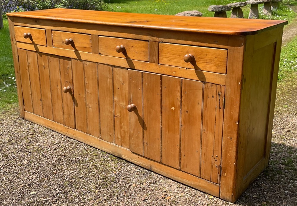 A long Victorian pine sideboard featuring four upper drawers above plank-fronted cupboard doors with turned wooden knobs.