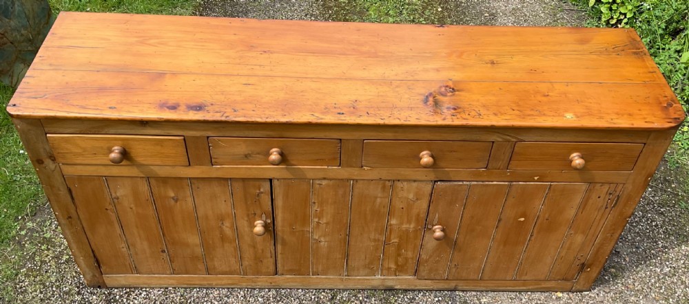 A long Victorian pine sideboard featuring four upper drawers above plank-fronted cupboard doors with turned wooden knobs. View V