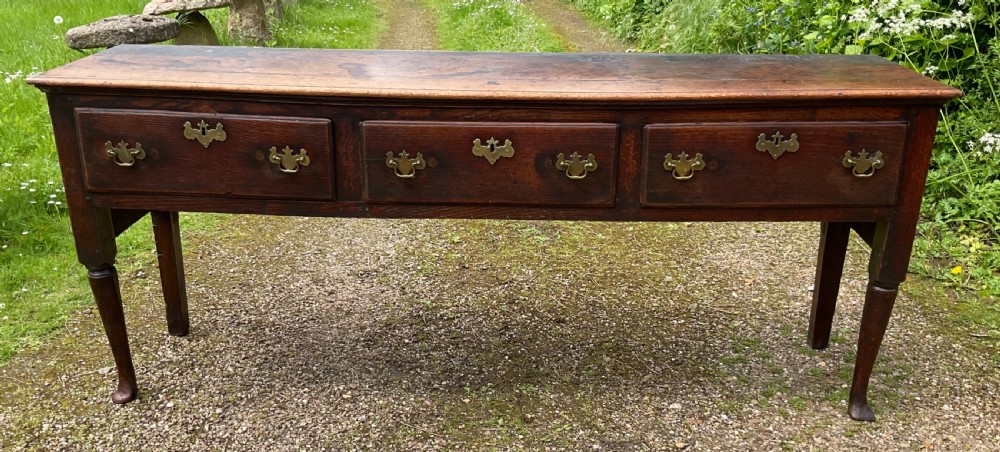 An 18th-century Georgian oak dresser base featuring three inline drawers with brass swan-neck handles, supported on slender turned legs with pad feet. View II