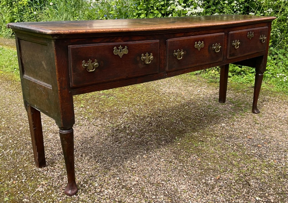 An 18th-century Georgian oak dresser base featuring three inline drawers with brass swan-neck handles, supported on slender turned legs with pad feet. View III