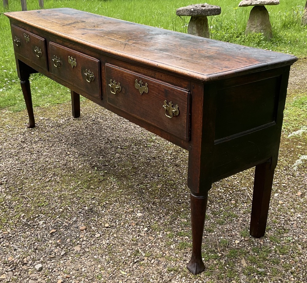 An 18th-century Georgian oak dresser base featuring three inline drawers with brass swan-neck handles, supported on slender turned legs with pad feet. View IV