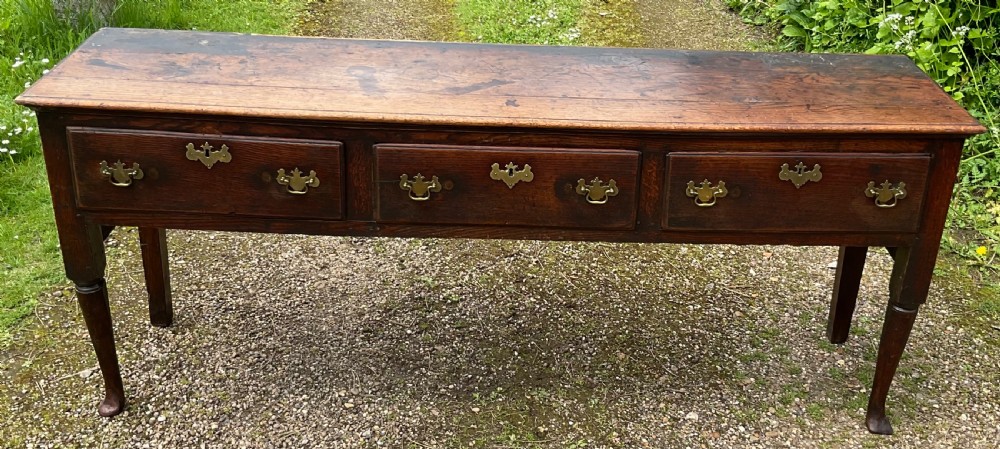 An 18th-century Georgian oak dresser base featuring three inline drawers with brass swan-neck handles, supported on slender turned legs with pad feet. View V