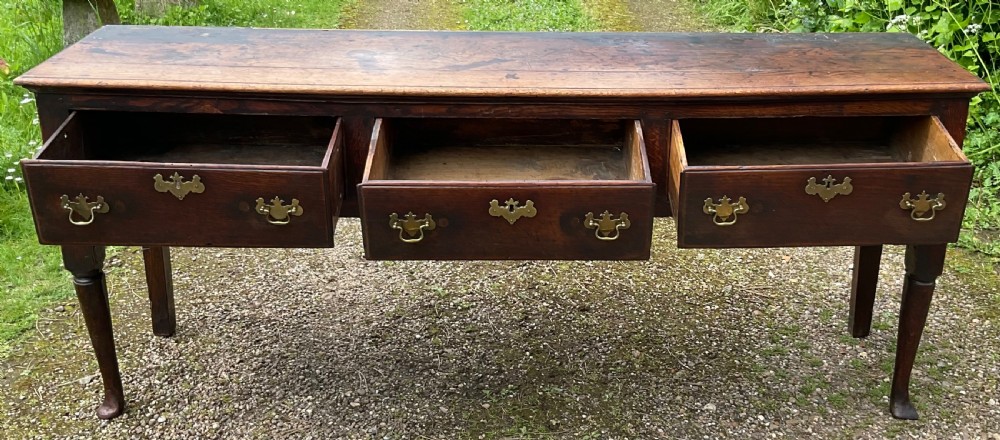An 18th-century Georgian oak dresser base featuring three inline drawers with brass swan-neck handles, supported on slender turned legs with pad feet. View VIII