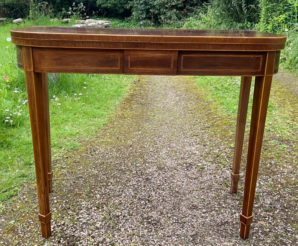 A Georgian inlaid mahogany foldover tea table featuring a rounded rectangular top, linear boxwood stringing, and square tapered legs.