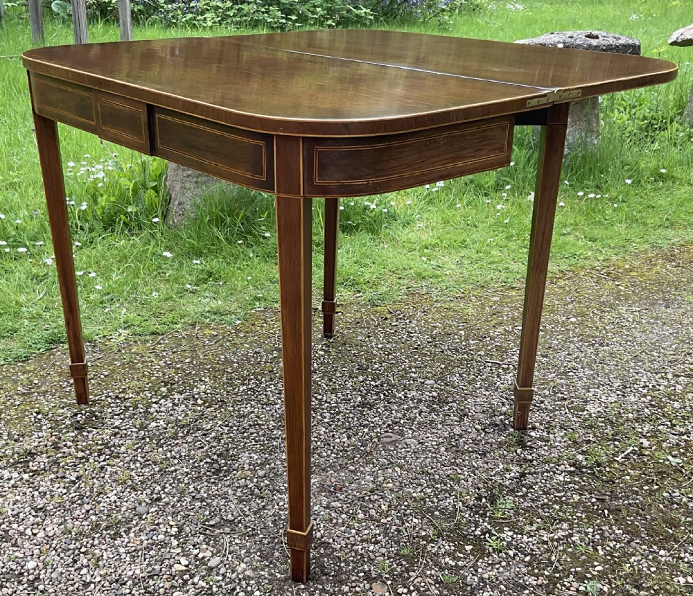 A Georgian inlaid mahogany foldover tea table featuring a rounded rectangular top, linear boxwood stringing, and square tapered legs. View VII