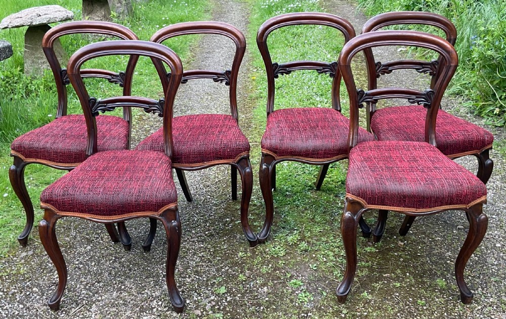 Set of six Victorian rosewood balloon back dining chairs featuring carved mid-rails, cabriole front legs, and red textured upholstered seats.