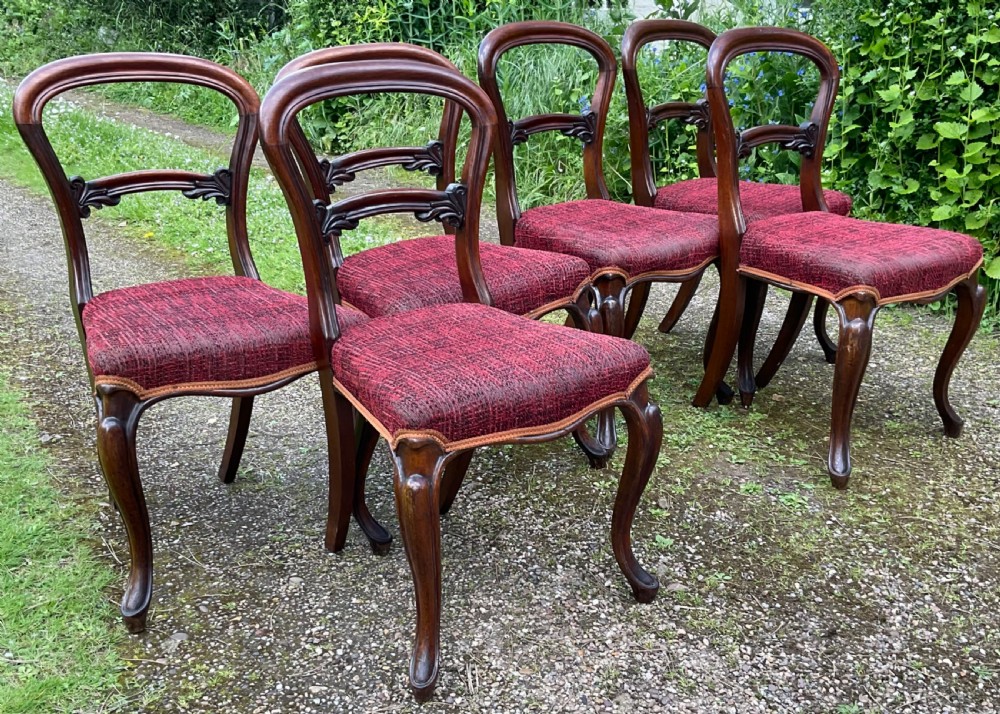 Set of six Victorian rosewood balloon back dining chairs featuring carved mid-rails, cabriole front legs, and red textured upholstered seats. View VI