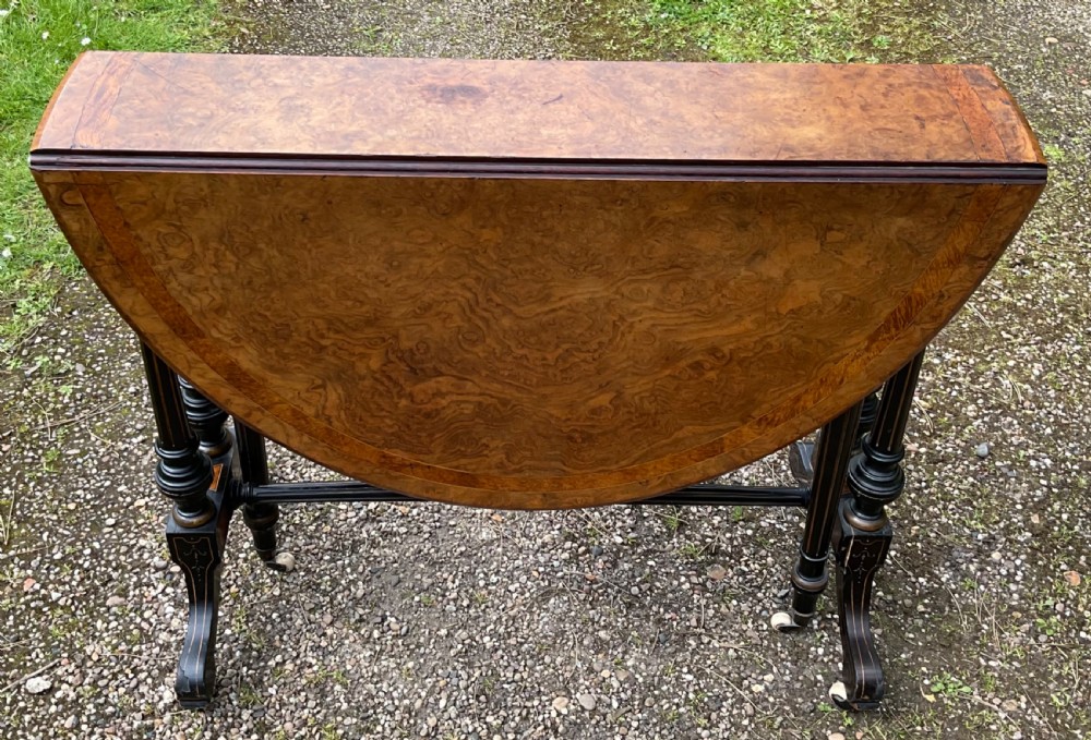 A Victorian drop-leaf table with a burr walnut oval top, ebonised turned legs, stretcher, and splayed feet on ceramic castors. View IV