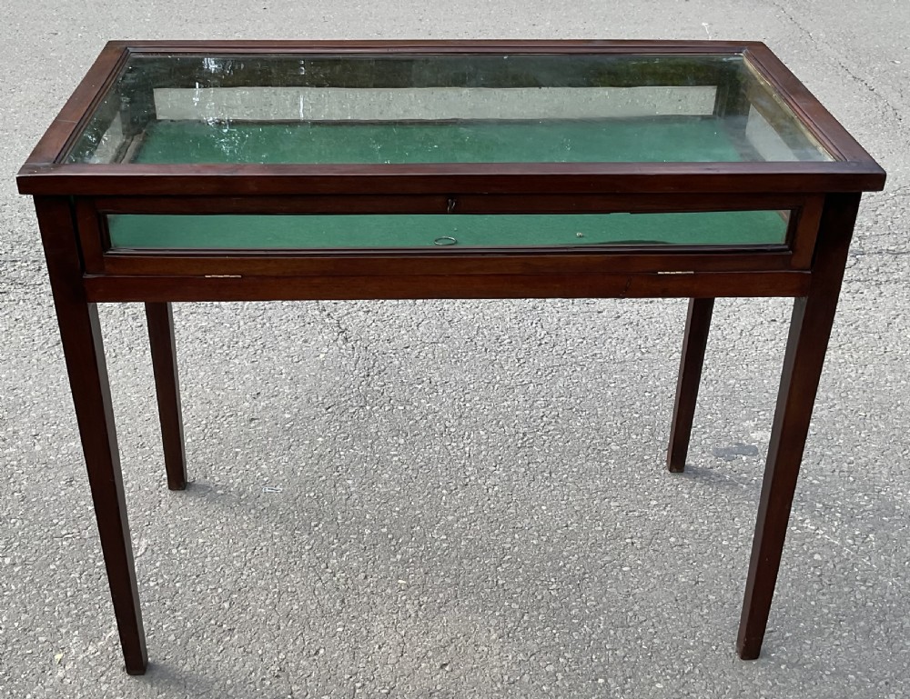 An Edwardian mahogany display table featuring a rectangular glass top, glazed sides, a green baize interior base, and slender square tapered legs.