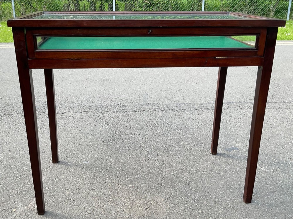 An Edwardian mahogany display table featuring a rectangular glass top, glazed sides, a green baize interior base, and slender square tapered legs. View III