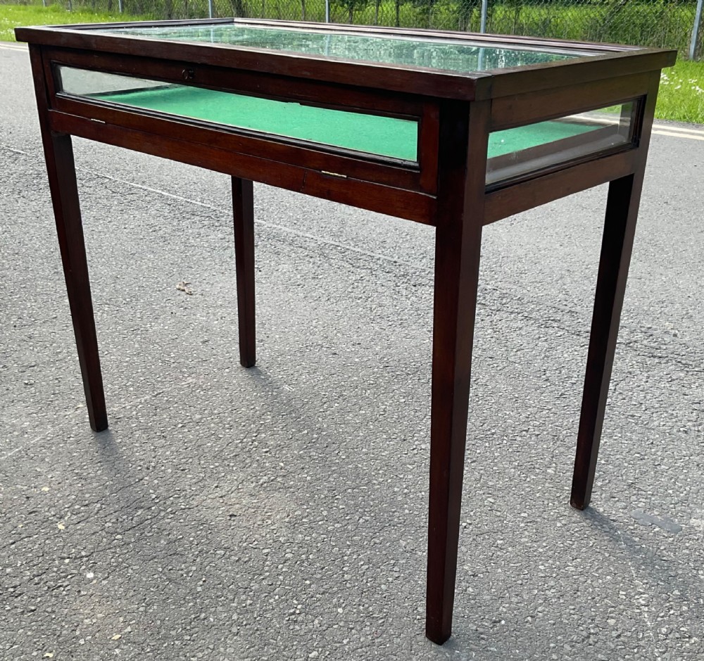 An Edwardian mahogany display table featuring a rectangular glass top, glazed sides, a green baize interior base, and slender square tapered legs. View IV